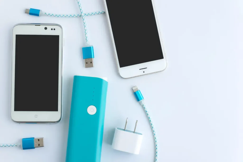 Dois smartphones, carregador portátil azul, cabos e adaptador dispostos em flat lay para loja de celular