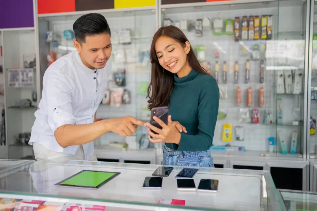 Vendedor mostrando smartphone para cliente sorridente em loja, explicando como vender celular usado