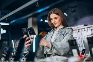 Jovem mulher escolhendo smartphone em loja de celular moderna com vitrines iluminadas e varios modelos expostos