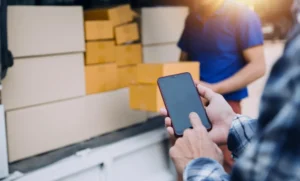 Pessoa usando smartphone para controlar estoque de celulares por IMEI ao lado de entregador com caixas em van de entrega