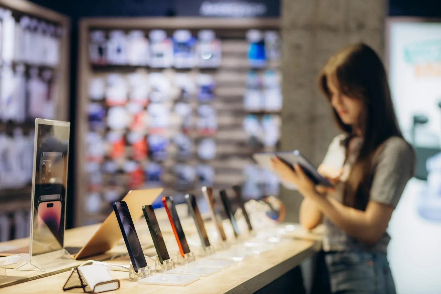 Cliente analisando smartphone em vitrine de loja de celular com varios aparelhos expostos e parede de acessorios ao fundo