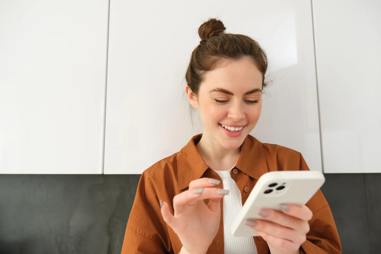 Mulher sorrindo enquanto usa smartphone branco para verificar IMEI do aparelho com fundo claro e neutro